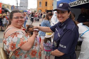 Na zdjęciu policjantka głaszcze małego pieska, którego trzyma na rękach kobieta.